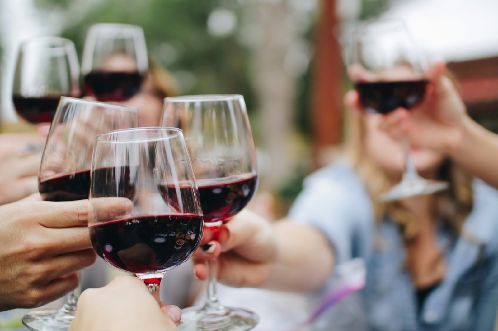 Friends raising glasses of red wine outdoors during golden hour